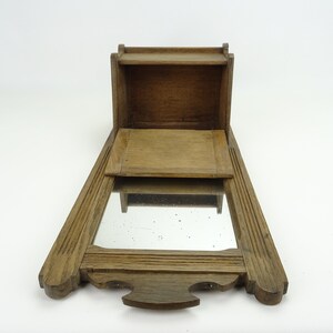 May include: A wooden wall-mounted mirror with a small shelf and a hinged door. The mirror is rectangular and has a simple frame. The shelf is open and the door is closed.