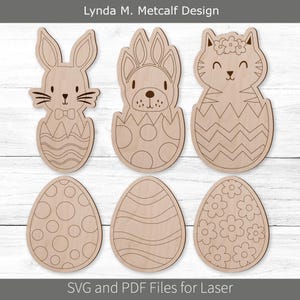 May include: Wooden Easter-themed cutouts featuring a bunny, a dog-like creature, and a cat, each emerging from an egg. Additional egg-shaped cutouts with various patterns are also included. The text "Lynda M. Metcalf Design" and "SVG and PDF Files for Laser" are visible.