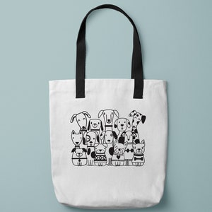 May include: A white tote bag with black handles and a black and white illustration of a group of dogs on the front. The illustration includes a variety of dog breeds, including a dalmatian, a pug, a bulldog, and a terrier. The text "Lynda M. Metcalf SVG Design" is printed below the illustration.