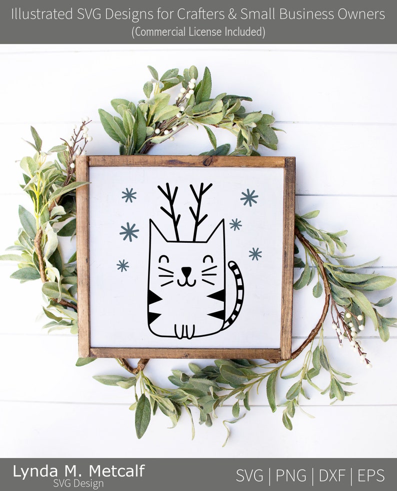 May include: A black and white illustration of a cat with antlers, surrounded by snowflakes. The cat is sitting on a white background inside a wooden frame.