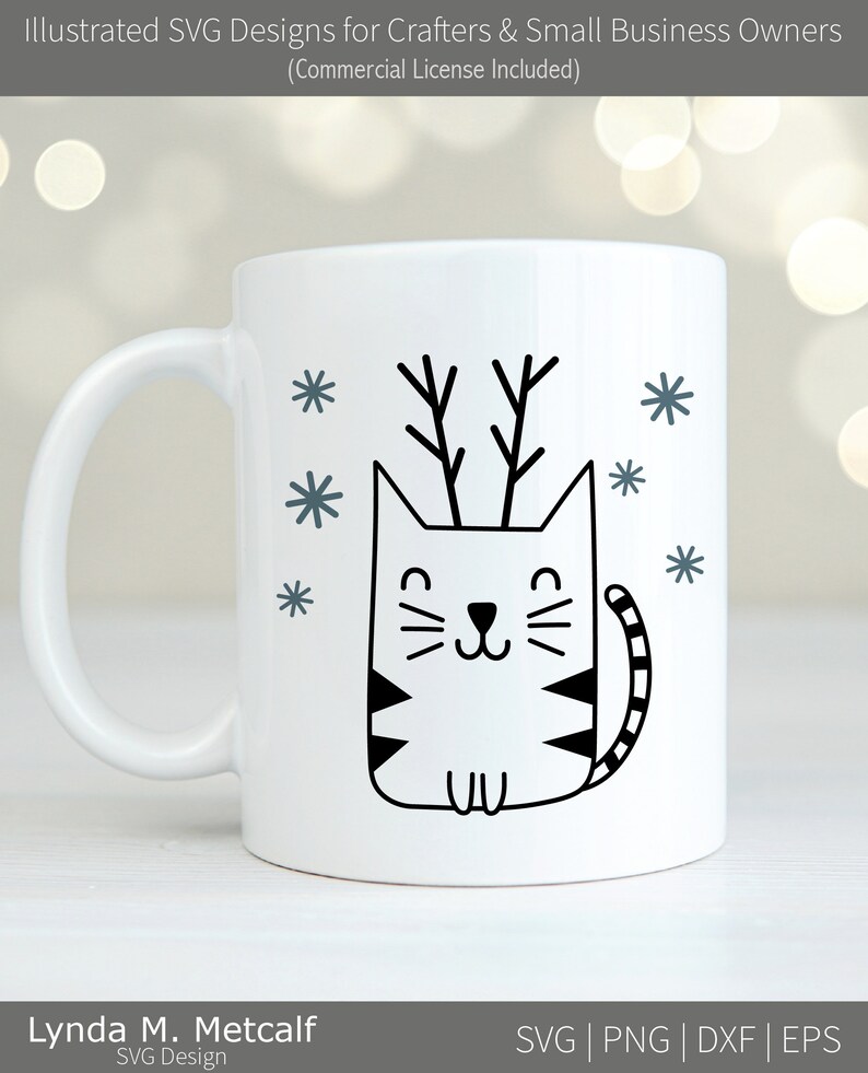 May include: White ceramic mug featuring a black and white illustration of a cat wearing antlers. The cat is surrounded by small snowflakes.