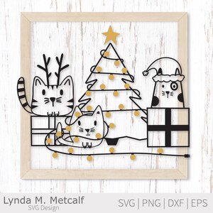K&ouml;nnte beinhalten: Ein gerahmtes Kunstwerk zum Thema Weihnachten mit drei stilisierten Katzen, einem Weihnachtsbaum und Geschenken. Die Katzen sind schwarz und wei&szlig;, eine tr&auml;gt ein Geweih und eine andere einen Weihnachtsm&uuml;tze. Der Baum ist mit gelben Lichtern und einem Stern geschm&uuml;ckt. Der Rahmen ist aus hellem Holz.
