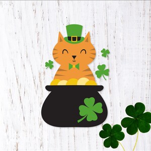 May include: An orange cat wearing a green leprechaun hat sits in a black pot filled with gold coins.  The cat is smiling and has a green bow tie.  There are four green shamrocks around the pot.