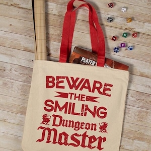 May include: A beige canvas tote bag with red handles and the text "Beware the Smiling Dungeon Master" printed in red.