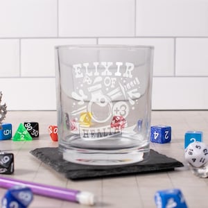 May include: A clear glass tumbler with an etched design of a potion bottle, dice, and the text "Elixir of Health +3".