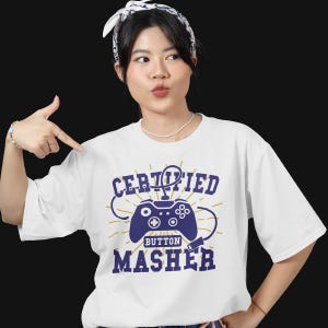 May include: White t-shirt with a blue and gold graphic of a video game controller and the text "CERTIFIED BUTTON MASHER".