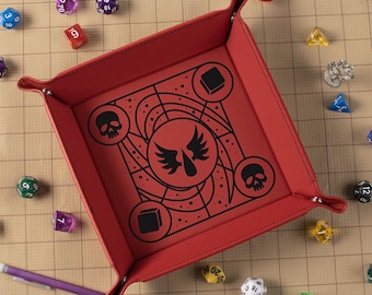 May include: A red, square dice tray with a black graphic design featuring skulls, wings, and geometric shapes. The tray is surrounded by various colorful dice, including D20s, D12s, and D6s. A purple pen rests near the tray.