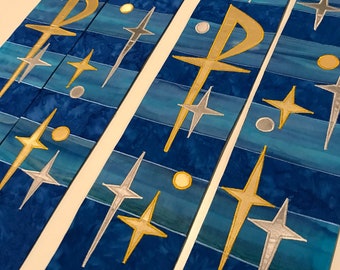 May include: Several blue fabric stoles with gold and silver embroidered crosses, stars, and the Chi Rho symbol. The stoles have a textured, marbled appearance with horizontal bands of lighter blue. The design is repeated across multiple stoles.
