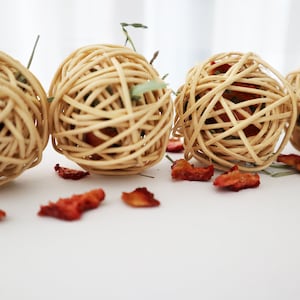 May include: Four woven wicker balls with dried fruit pieces scattered around them. The balls are light brown and have a natural, rustic look.