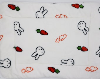Op de afbeelding: Witte huisdierbed met een witte rand en een herhalend patroon van zwarte konijnen en oranje wortels.