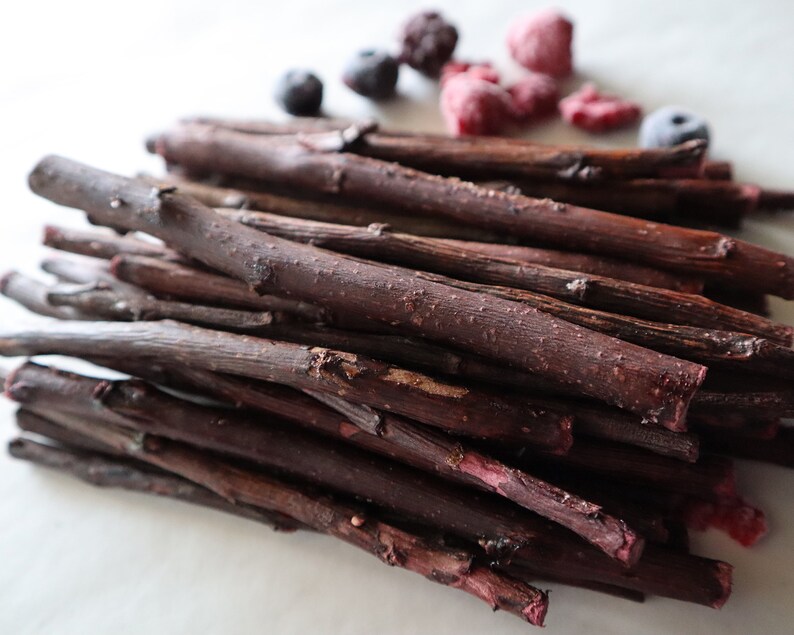 May include: A pile of thin, dark brown sticks with a reddish hue. The sticks are arranged in a random pattern and are all about the same length. There are some red and blue berries scattered around the sticks.