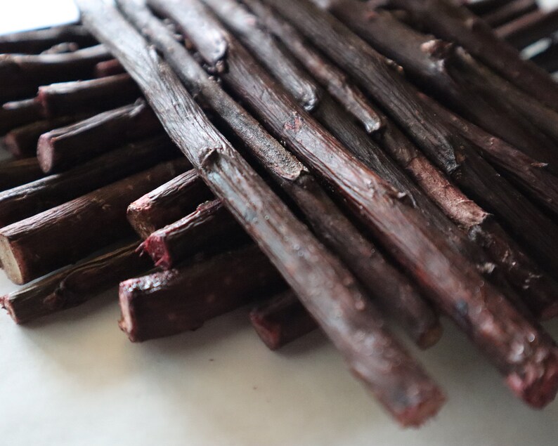 May include: A close-up of a bundle of dark brown sticks, some of which are slightly reddish in color. The sticks are arranged in a criss-cross pattern.