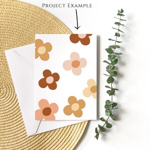 May include: A white card with a pattern of brown, pink, and orange flowers. The card is sitting on a woven straw mat.