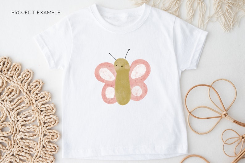 Puede incluir: Camiseta blanca con un gr&aacute;fico de mariposa rosa y verde. La mariposa tiene una cara sonriente y peque&ntilde;as antenas negras.