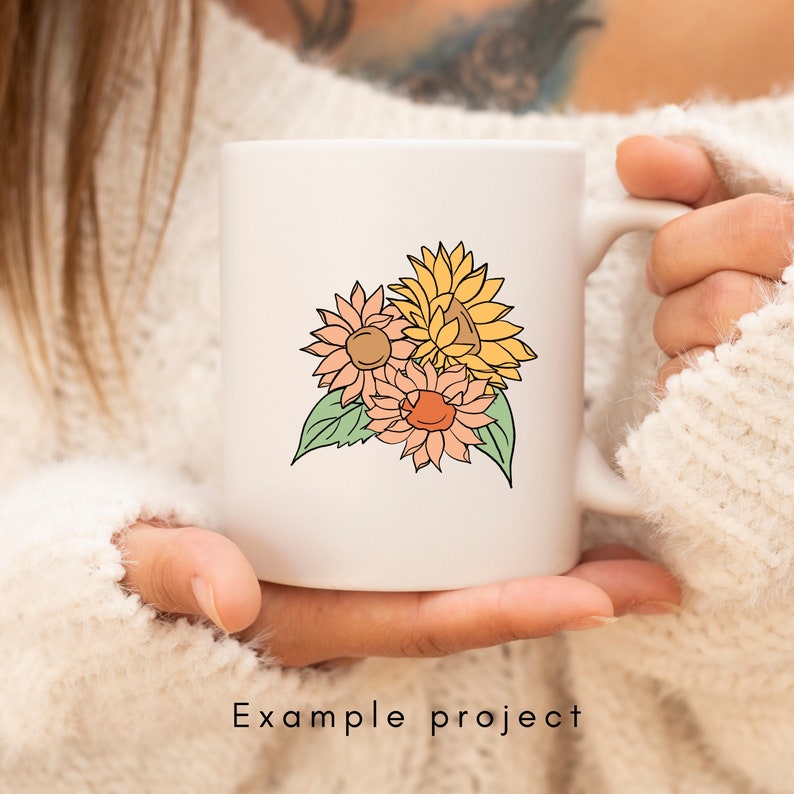 May include: White ceramic mug with a hand-drawn illustration of three sunflowers in shades of yellow, orange, and pink. The flowers are clustered together with green leaves.