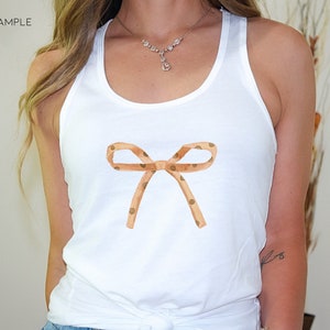 May include: White tank top with a brown and white polka dot bow on the front.