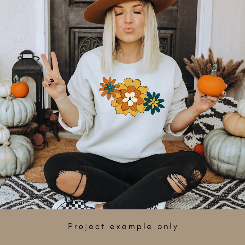 May include: A white sweatshirt with a colourful floral design on the front. The flowers are yellow, orange, green, and brown.