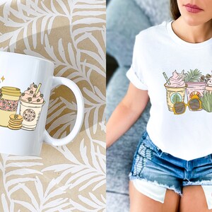 May include: White coffee mug with a handle featuring three illustrated iced coffee drinks with whipped cream and straws. The mug is on a patterned surface. A white t-shirt with the same design is also shown.