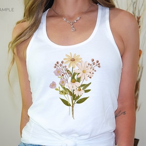 May include: A white tank top with a floral design featuring yellow, pink, and brown flowers. The flowers are arranged in a bouquet shape and are centered on the front of the tank top.