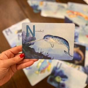 May include: A blue letter N with the word "narwhal" written below it. A watercolor illustration of a narwhal swimming in the ocean is shown on the card.