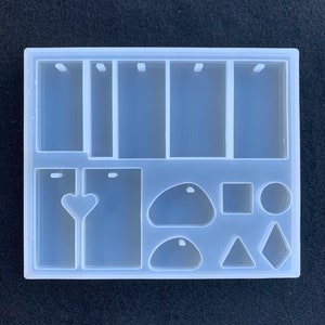May include: Clear silicone mold with multiple shapes for making resin jewelry. The mold includes six rectangular shapes with a hole at the top, two heart shapes, two oval shapes, a square, a circle, a triangle, and a diamond.