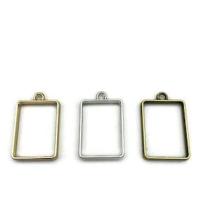 May include: Three metal pendant frames in gold, silver, and bronze. Each frame is rectangular with a rounded top and a loop for hanging.