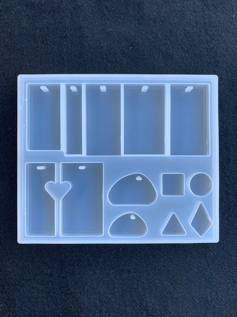 May include: Clear silicone mold with multiple shapes for making resin jewelry. The mold includes six rectangular shapes with a hole at the top, two heart shapes, two oval shapes, a square, a circle, a triangle, and a diamond.