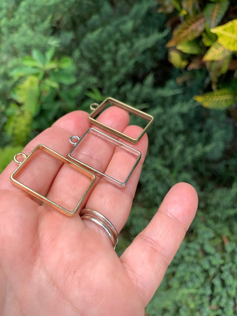 K&ouml;nnte beinhalten: Drei Metallbilderrahmen mit einer &Ouml;se oben zum Aufh&auml;ngen. Die Rahmen sind golden, silbern und bronzefarben.