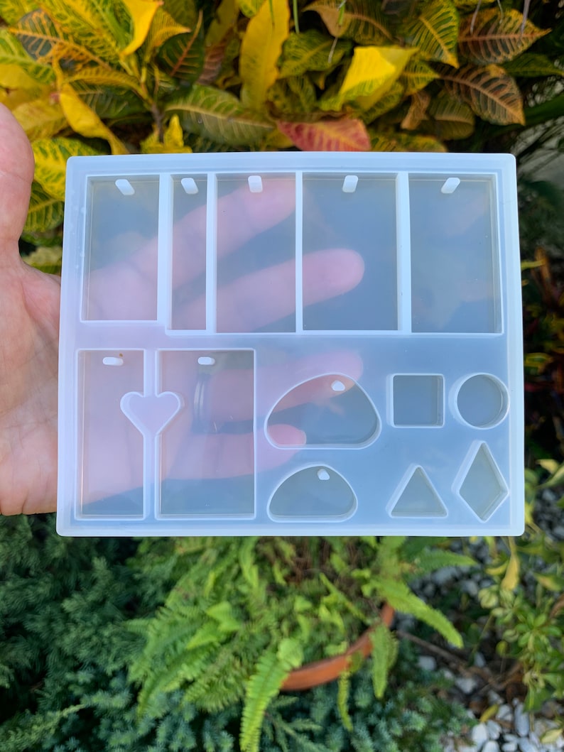 May include: Clear silicone mold with multiple shapes for making resin jewelry. The mold includes rectangular, heart, oval, round, square, and triangular shapes.