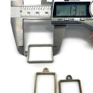 K&ouml;nnte beinhalten: Drei Metallrahmen f&uuml;r Harz-Kunst, einer silber, einer gold und einer bronze. Der silberne Rahmen wird mit einer Schieblehre gemessen, die eine Messung von 3,34 cm anzeigt.