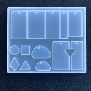 May include: Clear silicone mold with multiple shapes for resin casting. Includes rectangular, round, oval, heart, diamond, and triangle shapes. Also includes four rectangular molds with two holes each.