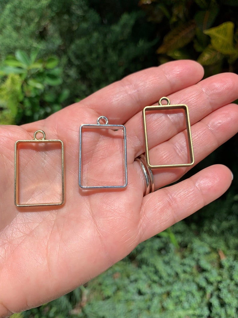 K&ouml;nnte beinhalten: Drei Metall-Anh&auml;nger-Rahmen in Gold, Silber und Bronze. Jeder Rahmen ist rechteckig mit einer kleinen Schlaufe oben zum Aufh&auml;ngen.