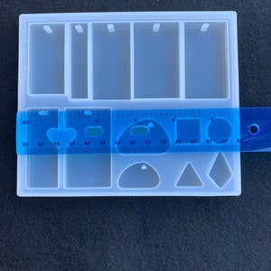 May include: A clear silicone mold for making jewelry. The mold has six rectangular spaces for making pendants, a space for making a teardrop shape, a triangle shape, and a square shape. The mold is 5 inches wide and 3 inches long.
