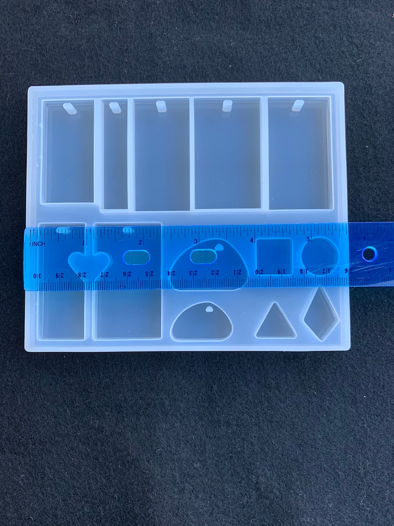 May include: A clear silicone mold for making jewelry. The mold has six rectangular spaces for making pendants, a space for making a teardrop shape, a triangle shape, and a square shape. The mold is 5 inches wide and 3 inches long.
