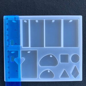 May include: A white silicone mold with nine different shapes for making jewelry. The mold includes three rectangular shapes with holes for hanging, a large teardrop shape, a small teardrop shape, a round shape, a square shape, a triangle shape, and a diamond shape.