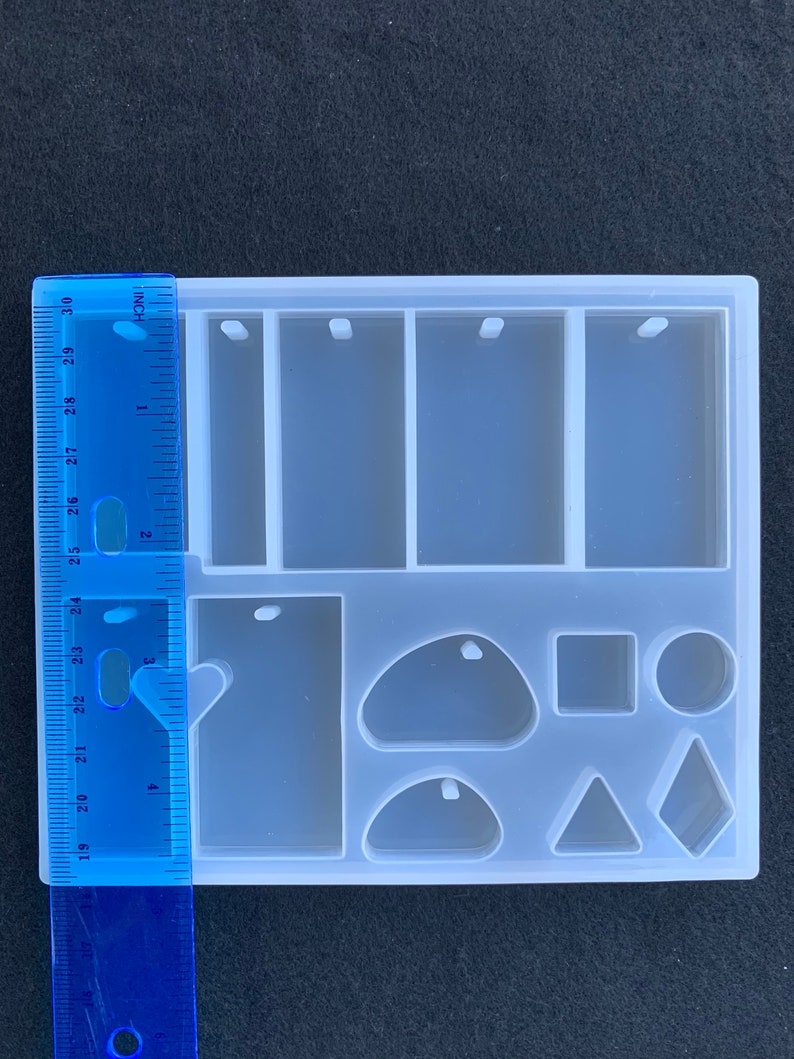 May include: A white silicone mold with nine different shapes for making jewelry. The mold includes three rectangular shapes with holes for hanging, a large teardrop shape, a small teardrop shape, a round shape, a square shape, a triangle shape, and a diamond shape.