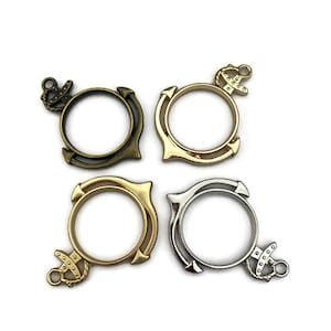 May include: Four anchor-shaped metal rings in gold, bronze, and silver. The rings are open and have a smooth, polished finish.