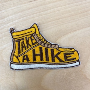 May include: Yellow embroidered patch of a hiking boot with the text "Take a Hike" in brown thread.