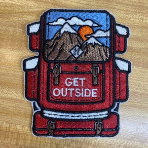 May include: Embroidered patch featuring a red backpack design with the text "GET OUTSIDE". The backpack has a scenic view of mountains, a sun, and clouds. The patch has white, brown, blue, and orange accents, and is suitable for outdoor enthusiasts.
