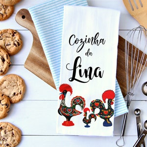 May include: White kitchen towel with the text "Cozinha da Lina" in black cursive lettering. Two colorful rooster illustrations are at the bottom of the towel.