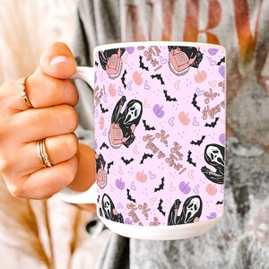 May include: A white ceramic mug with a pink background and a repeating pattern of a ghost holding a phone, bats, hearts, and pumpkins. The text on the mug reads "No, you hang up first!"