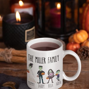Może przedstawiać: Biały kubek ceramiczny z czarno-białym rysunkiem rodziny ubranej w kostiumy na Halloween. Na kubku nadrukowany jest tekst "The Miller Family". Pod rysunkiem nadrukowane są imiona "Mommy", "Daddy", "Bella" i "Aiden".