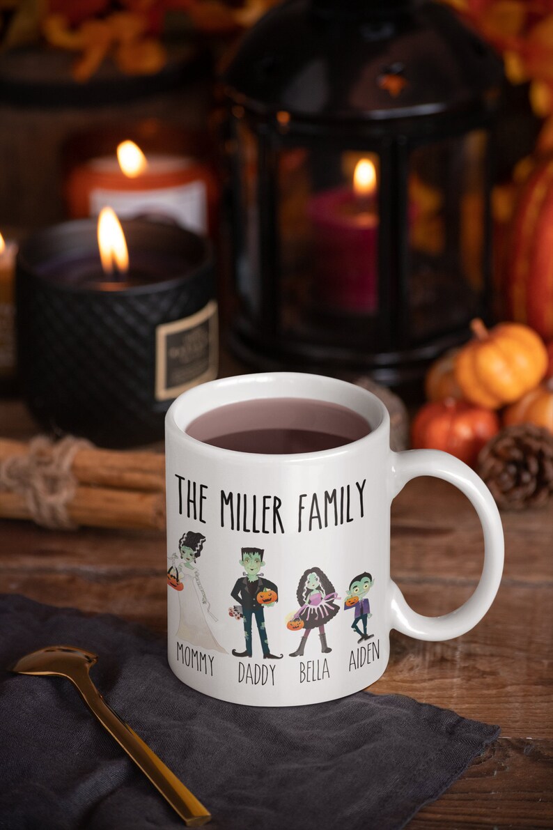 Może przedstawiać: Biały kubek ceramiczny z czarno-białym rysunkiem rodziny ubranej w kostiumy na Halloween. Na kubku nadrukowany jest tekst "The Miller Family". Pod rysunkiem nadrukowane są imiona "Mommy", "Daddy", "Bella" i "Aiden".
