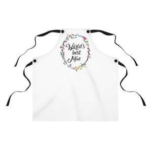 May include: White apron with black straps and a floral wreath design. The wreath has the text "World's best M&atilde;e" in black script.