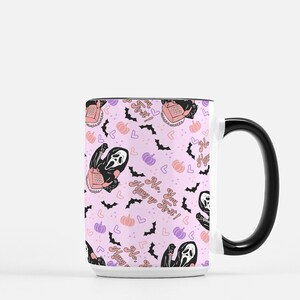 May include: White ceramic mug with a black handle. The mug features a pink background with a repeating pattern of a ghost holding a phone, bats, hearts, and pumpkins. The text "No, you hang up first!" is repeated throughout the pattern.