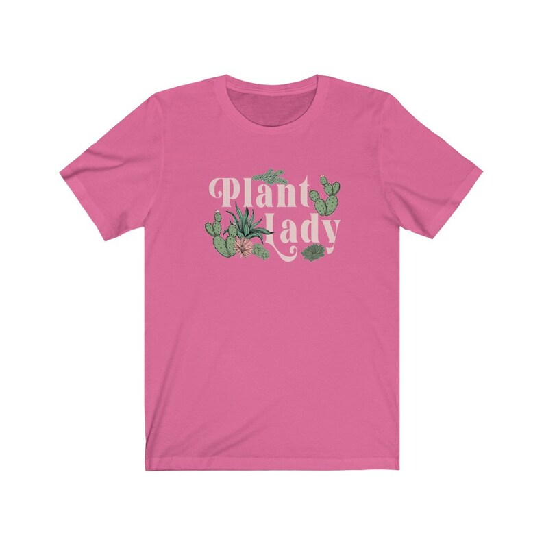 May include: Pink short-sleeved t-shirt with the text "Plant Lady" in a retro font. The text is surrounded by a variety of green plants, including cacti and succulents.
