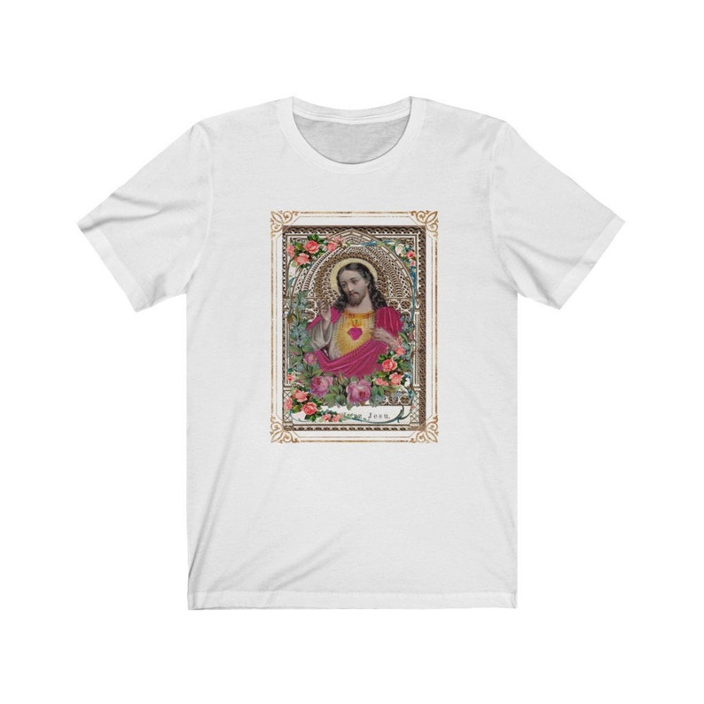 May include: White t-shirt with a vintage image of Jesus with a heart in his hand. The image is surrounded by a gold frame with floral details. The text "Jesus" is at the bottom of the image.