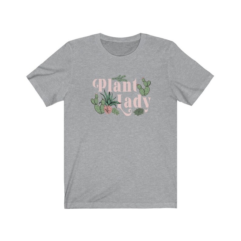 May include: A heather grey t-shirt with a pink graphic that says "Plant Lady" with a variety of green cacti and succulents surrounding the text.