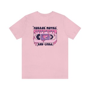 May include: Pink t-shirt with a graphic of a VHS tape dripping pink slime. The tape has a skull and heart design and the text "HORROR MOVIES AND CHILL".
