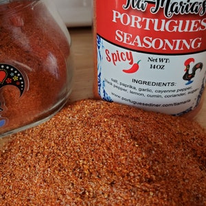 May include: A red and white jar filled with a red spice blend. The jar is labeled "Tia Maria's Portuguese Seasoning Spicy" and lists the ingredients: salt, paprika, garlic, cayenne pepper, black pepper, lemon, cumin, coriander, and sugar. The jar is 14 ounces.